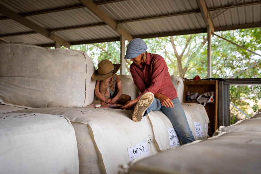 Photo of a woman reading a book to a child around wool bales.