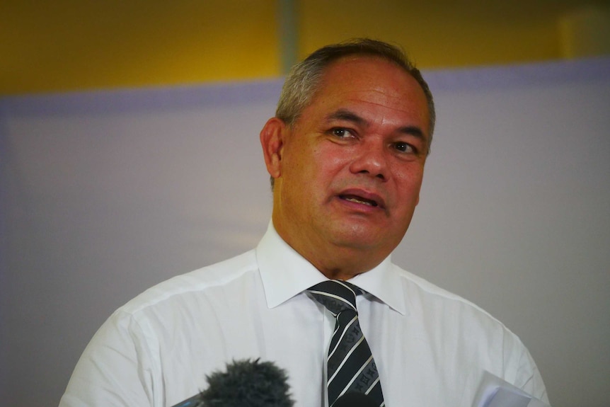 A ruddy man of late middle age, wearing a shirt and tie, speaking to the media.