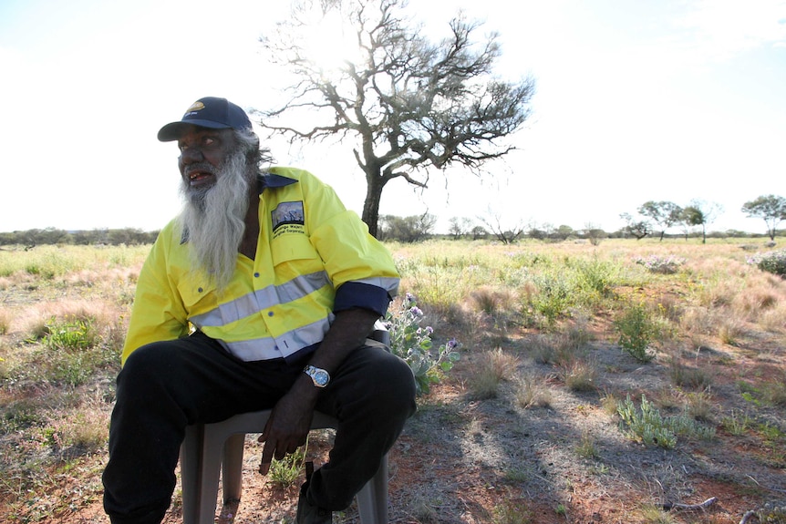 A man sits on a chair in the desert.