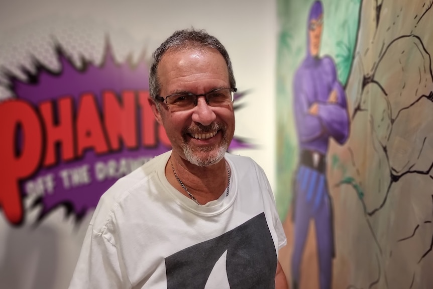 A man standing in front of a mural with a giant purple starburst with the word Phantom in  it.