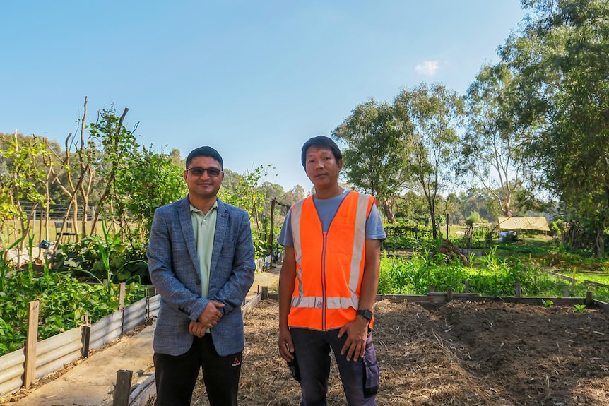 Harka Bista and DInesh stand in front of raised garden beds in the community farm.