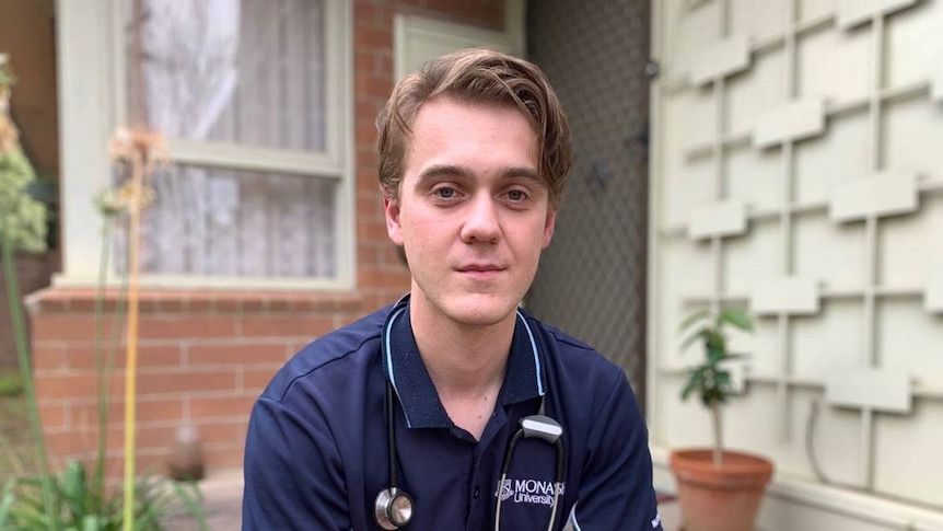 A young man wearing a Monash University t-shirt with a stethoscope around his neck