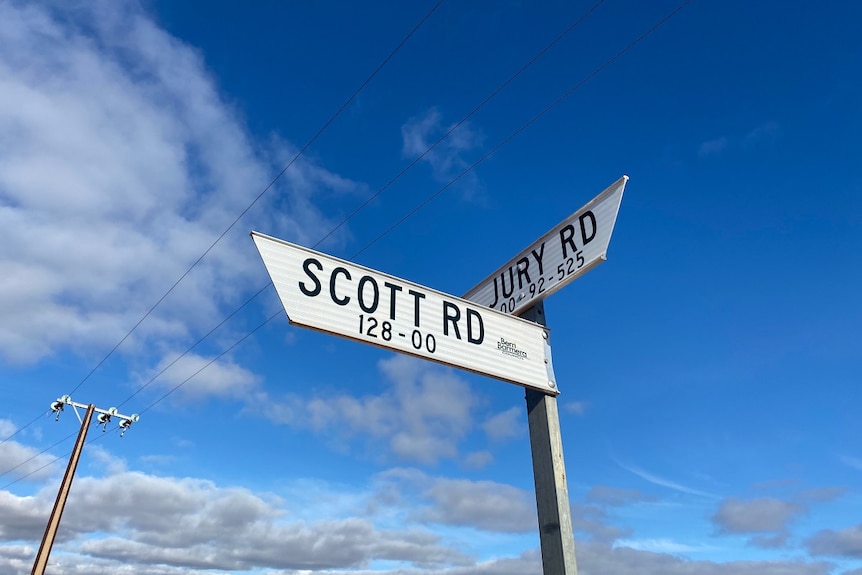 Two white road signs pointing at different 90 degree angles. One reads Scott Road and the other Jury Road.