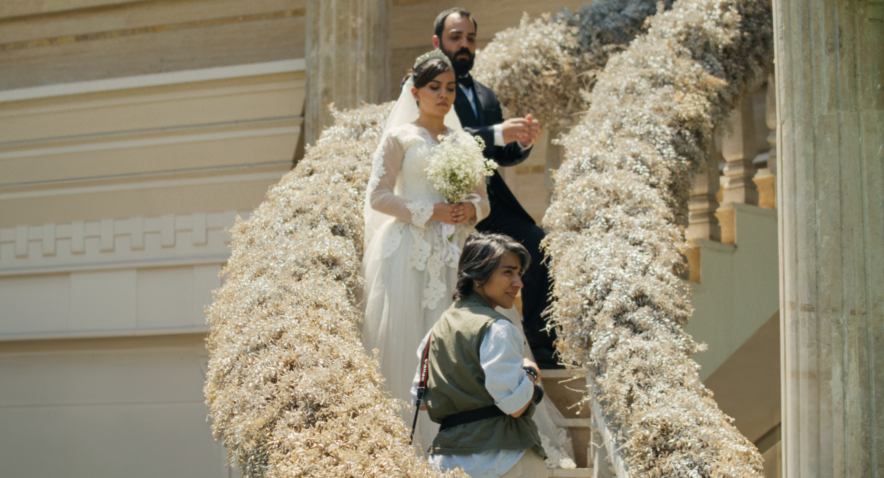 Os noivos descem uma escadaria coberta de flores com um fotógrafo