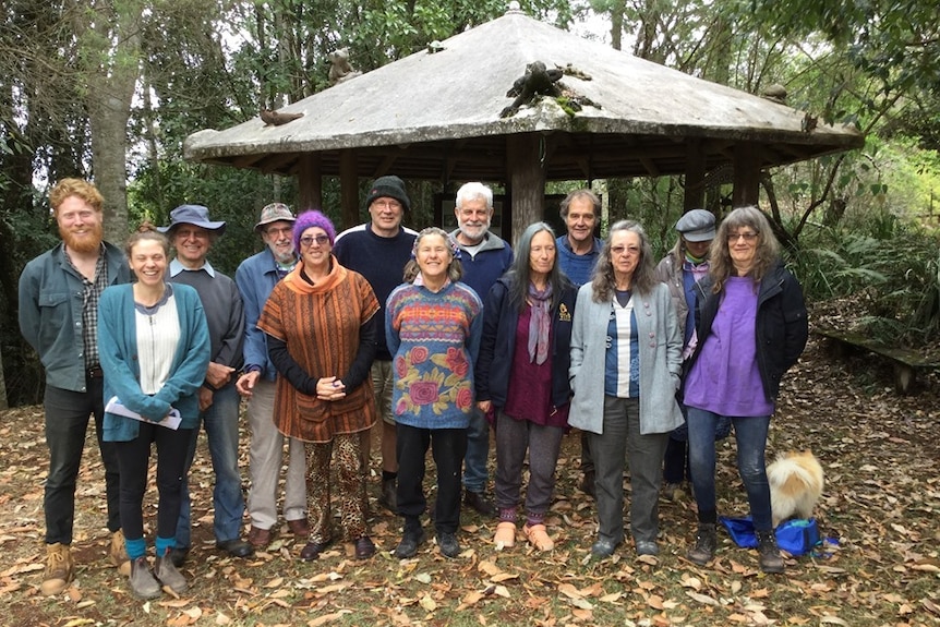 A recent group shot of hippy looking people standing in front of a rotunda with a backdrop of green trees