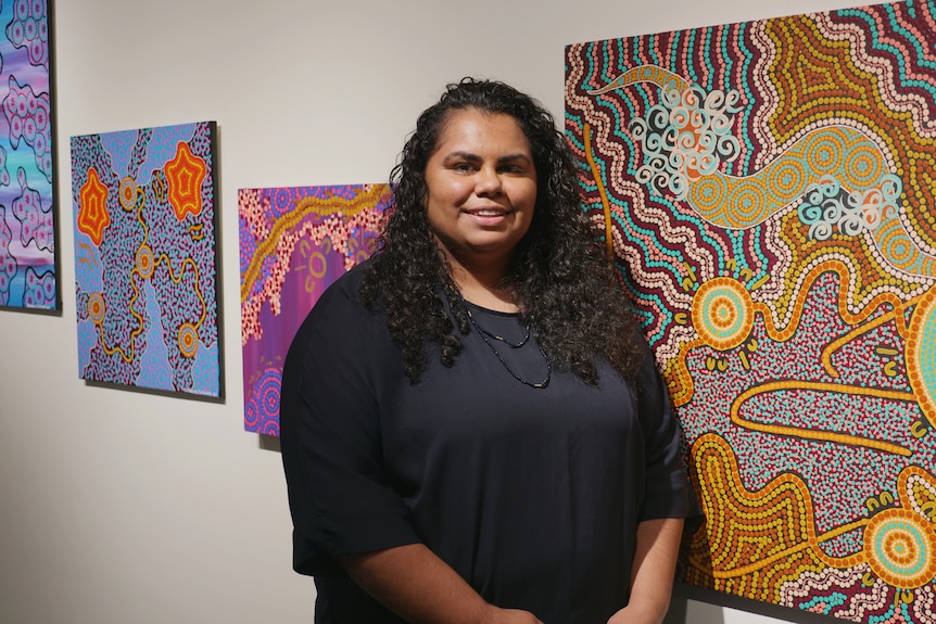 a woman standing and smiling in front of her artworks