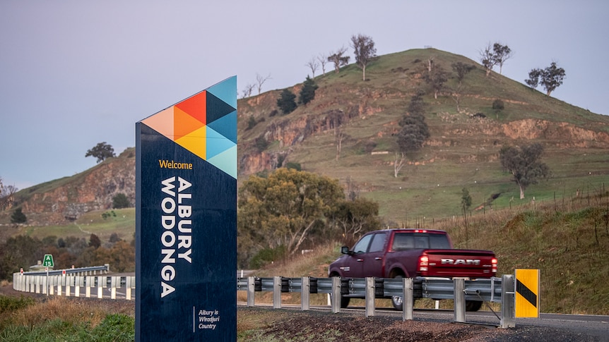 A car drives past a sign saying welcome to albury wodonga on a country road.