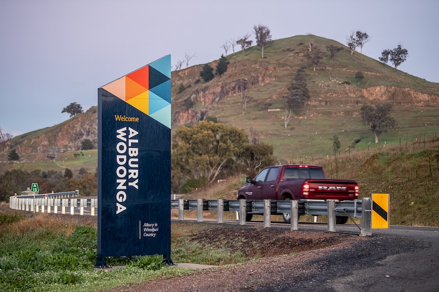 A car drives past a sign saying welcome to albury wodonga on a country road.