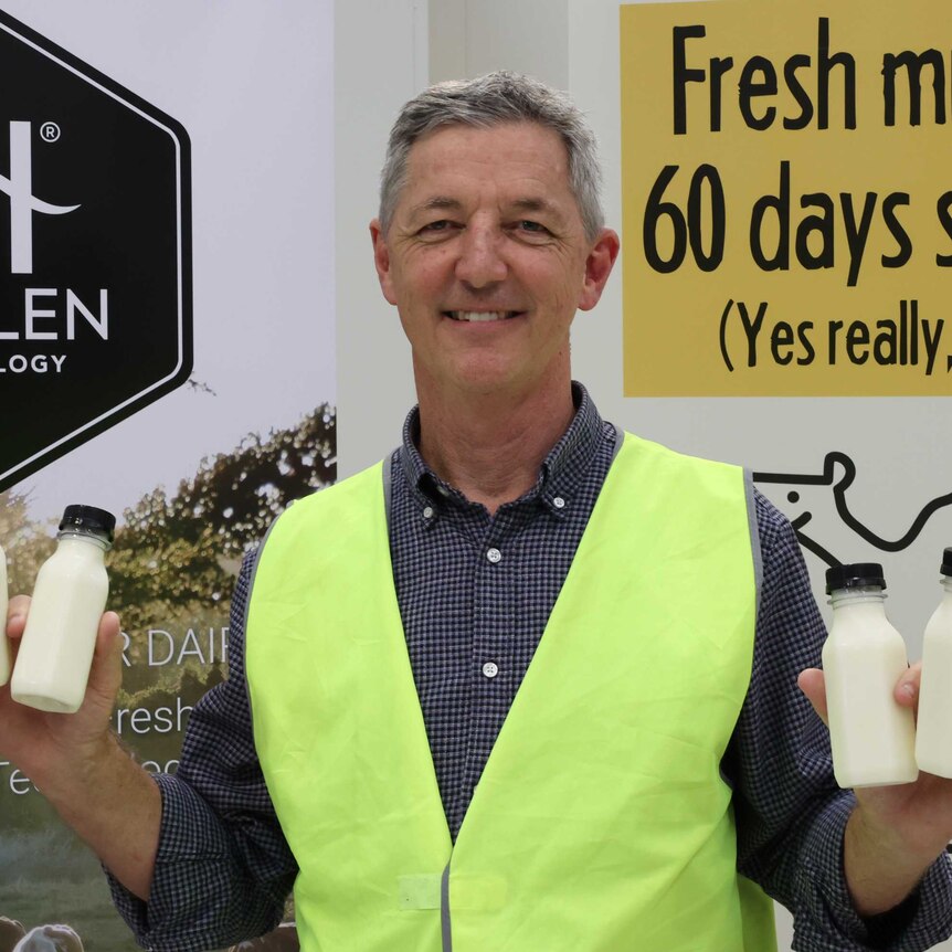 Inventor Jeff Hastings in fluoro vest holds up four small bottles of unlabelled milk in front of a sign saying Halen Technology.