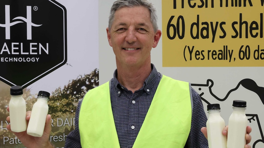 Inventor Jeff Hastings in fluoro vest holds up four small bottles of unlabelled milk in front of a sign saying Halen Technology.