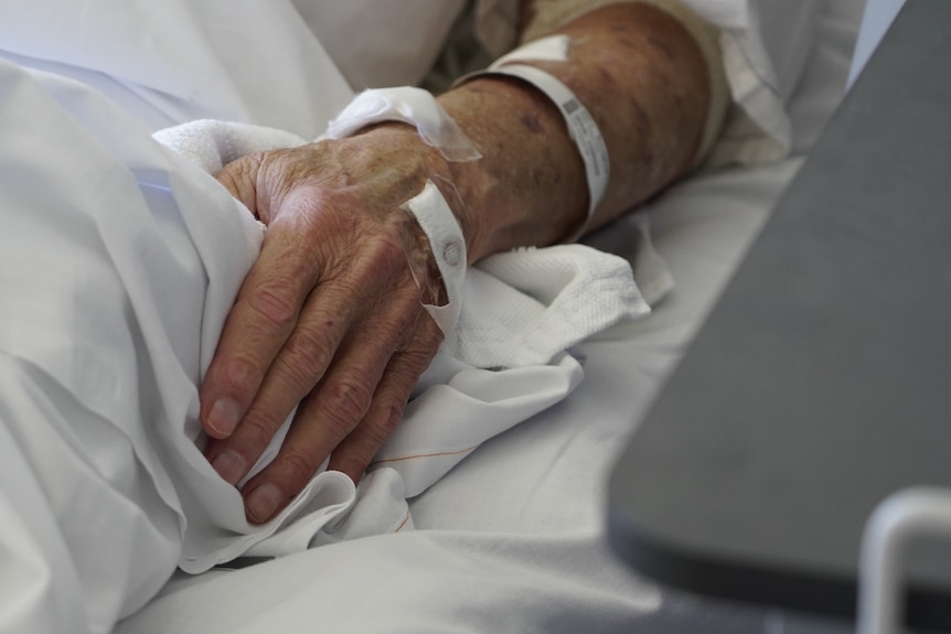 A photo of an older person's hand in a hospital bed
