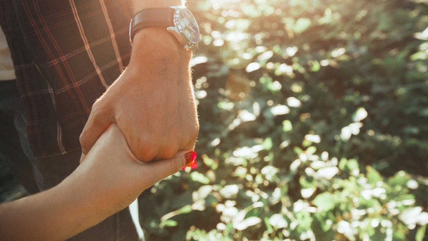 Anonymous man and woman hold hands in the forest in dappled sunlight.