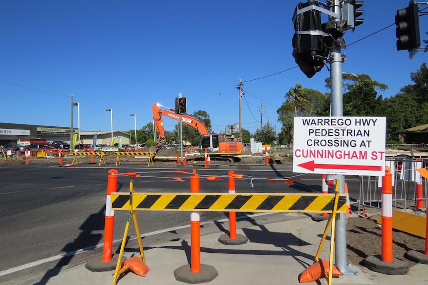 A pedestrian crossing is blocked with signs and poles, while a crane works in the background.