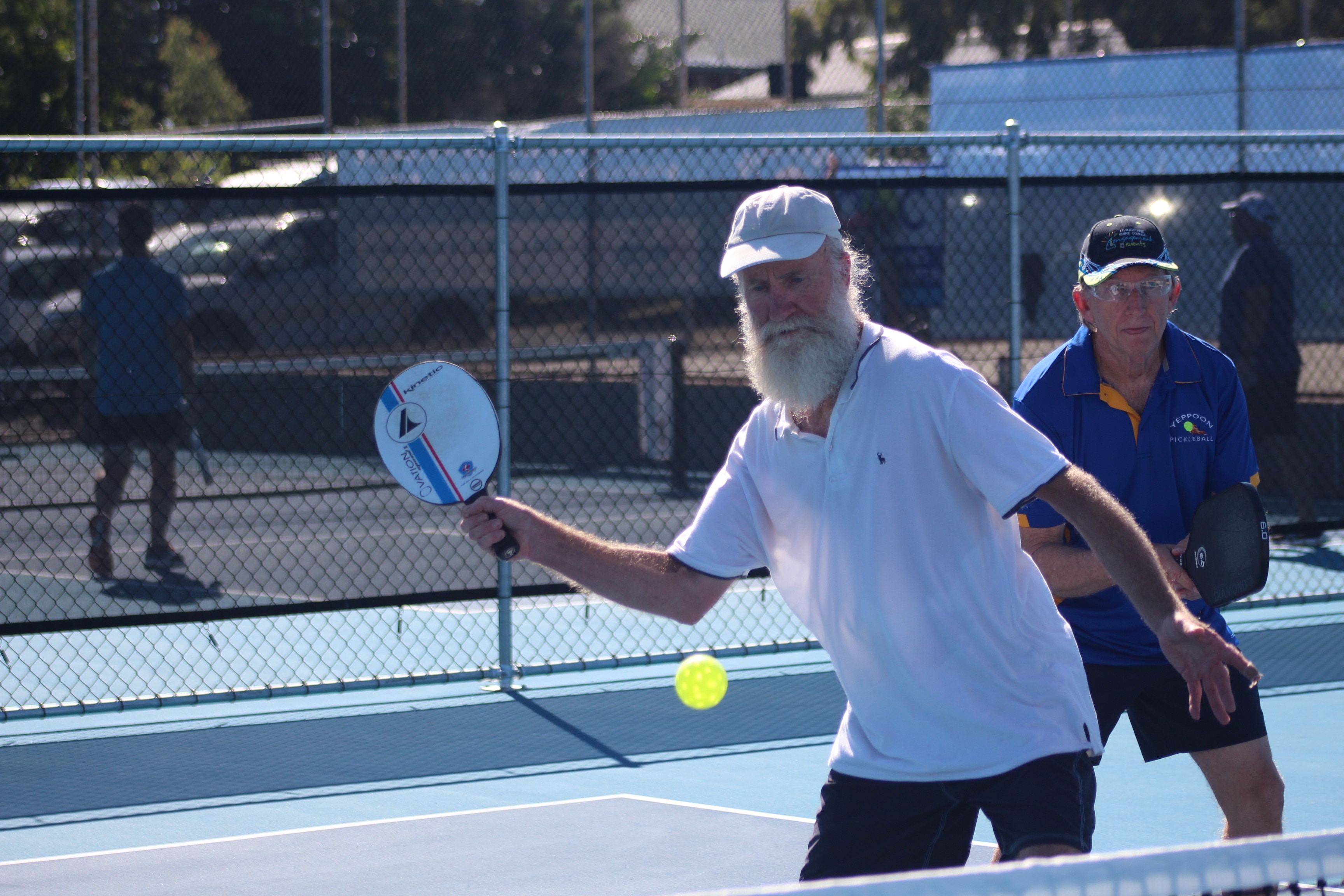 Two older men playing pickleball with one man attempting to strike the plastic ball with his paddle