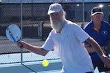 Two older men playing pickleball with one man attempting to strike the plastic ball with his paddle.