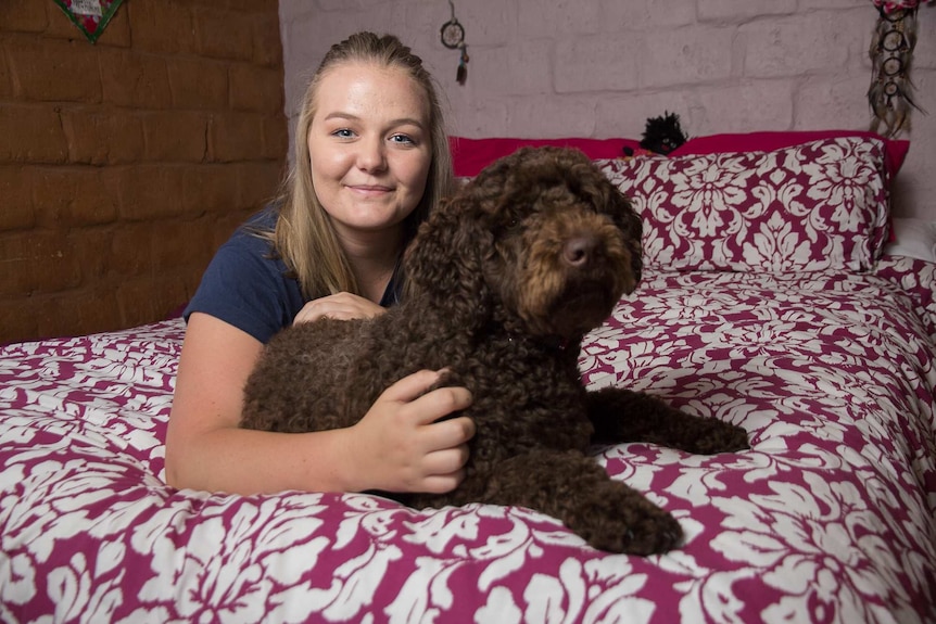 A woman and a brown curly haired dog on a bed