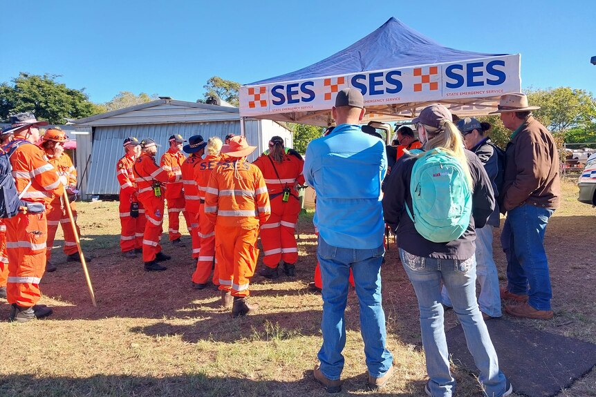 SES volunteers stand outside a tent receiving a briefing.