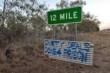 A sign for 12 Mile has a hand made sign beneath it stating "Dirty Deals Done 4 Prison"