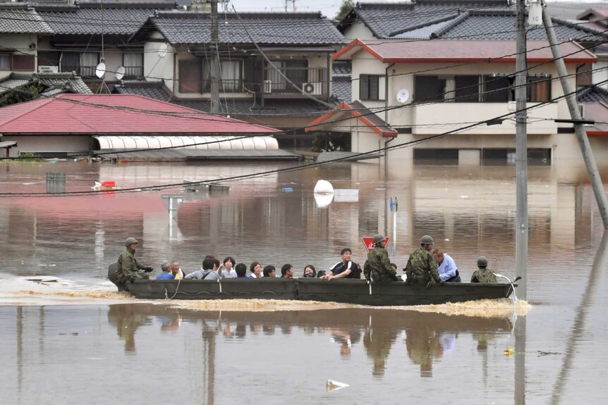Wide shot of a boat full of people streaming across floodwaters.