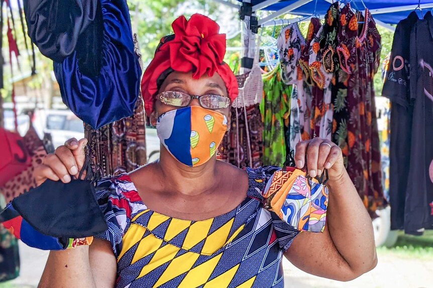 A woman in a brightly coloured dress at a market holding up face masks