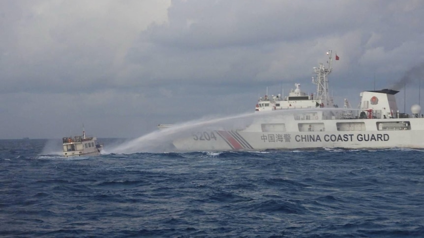 一艘涂有中国海警标志的白色船只向附近的木船喷射水柱