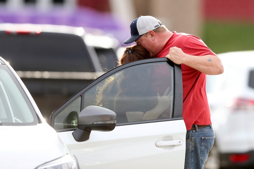 A man and a woman hug next to a car. 