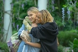 Black woman in her 20s with bleached braids embracing white women in her 20s wearing a blue top. 