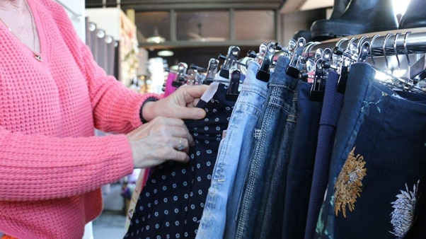 A hand of a woman in a pink jumper pulls out a pair of pants on a rack