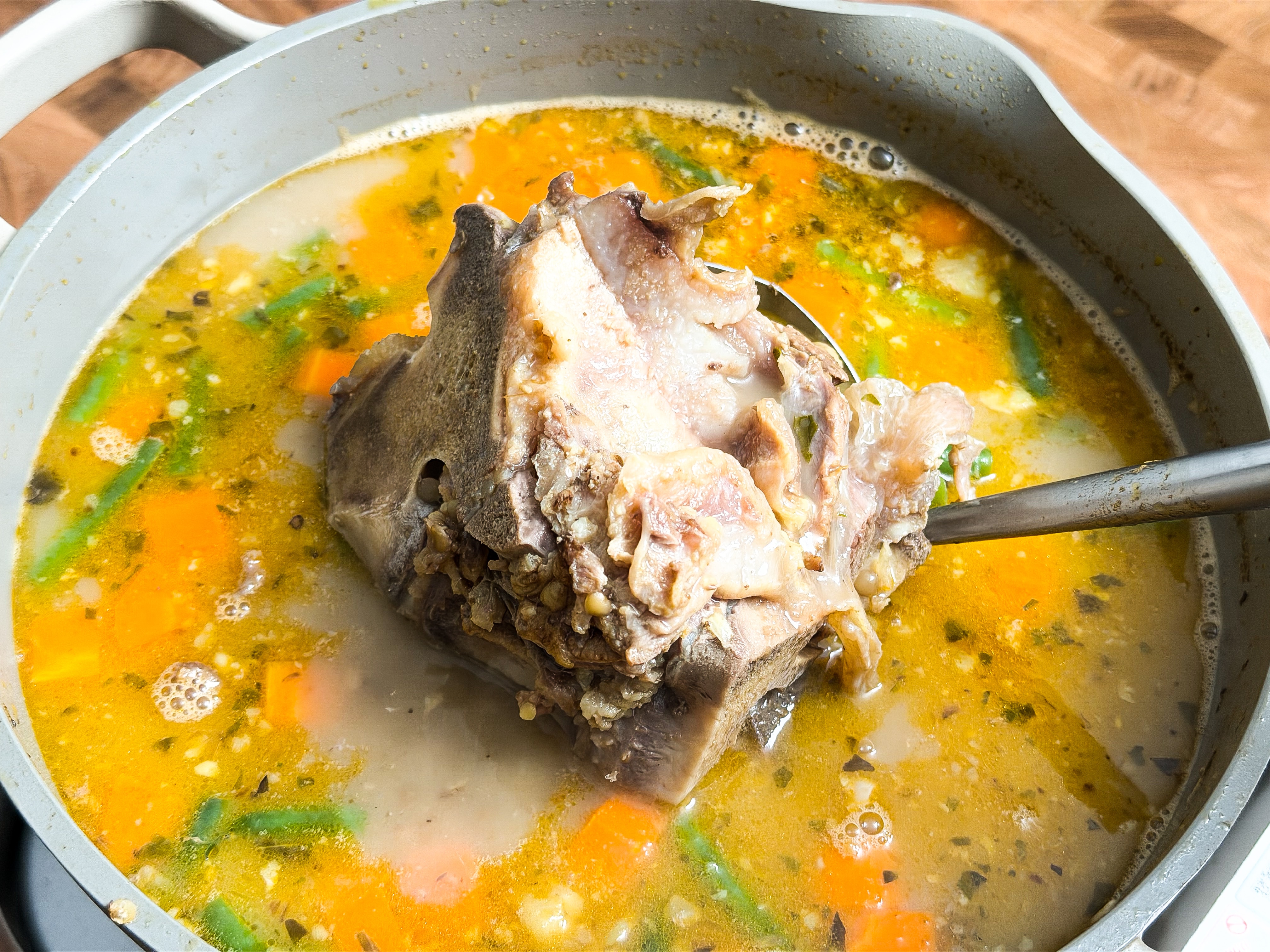 A large pot of broth with vegetables and a large beef bone in it.