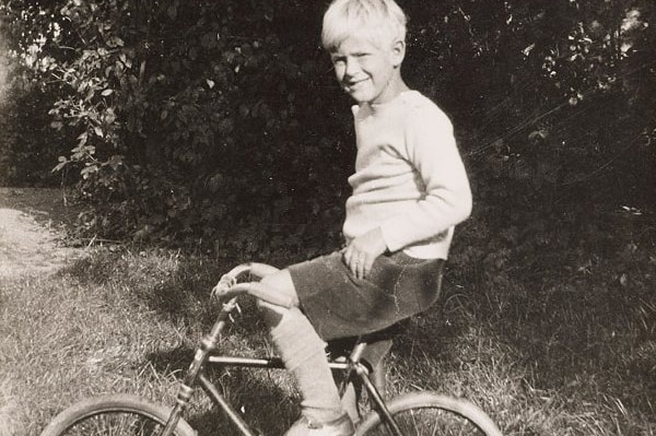 A black and white photo of a young boy sitting on a bicycle.