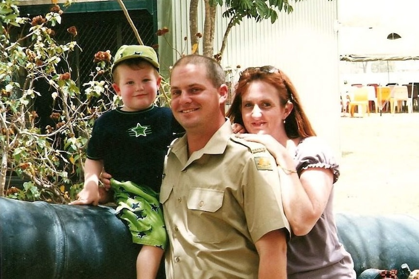 A small child, man and woman, leaning in and smiling for a picture together sitting on a cannon.