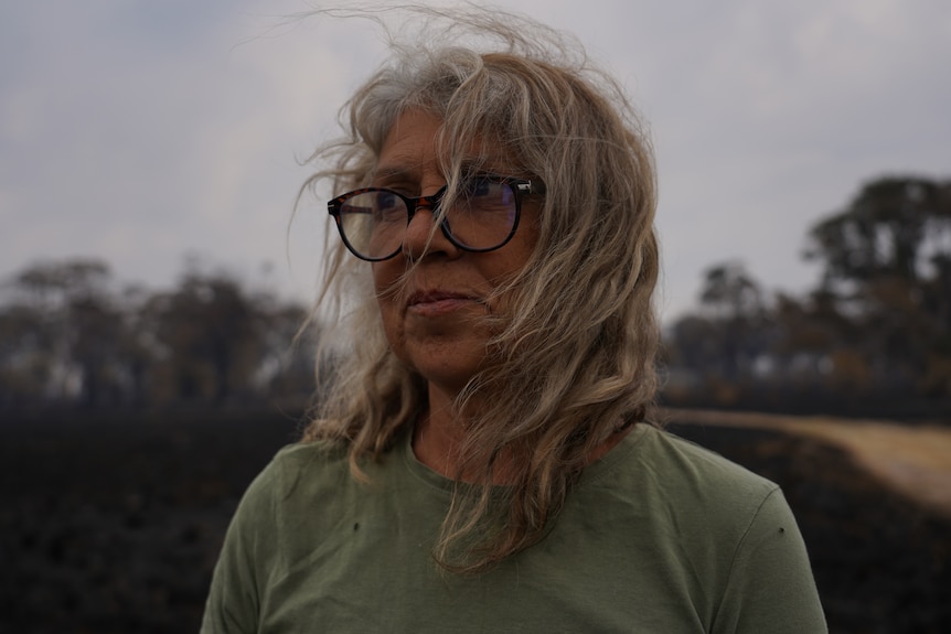 A woman standing in a burnt out farm.
