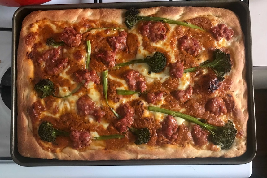 A rectangular homemade pizza on the stove top with broccolini, tomato sauce and cheese, a Sunday late lunch.