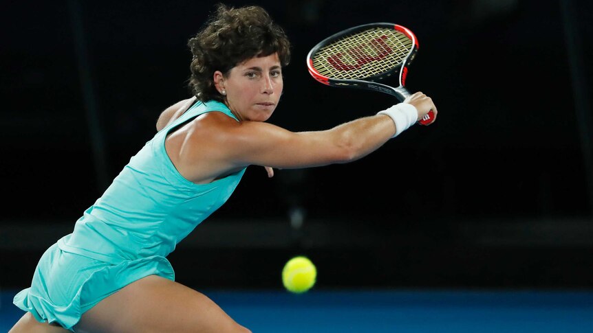 Carla Suarez Navarro looks at a tennis ball and reaches with her racquet in her right hand, about to play a backhand shot