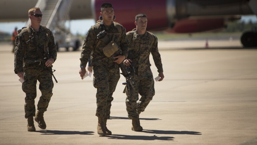 Three marines in uniform walk across the tarmac