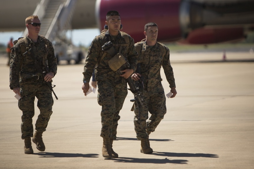 Three marines in uniform walk across the tarmac