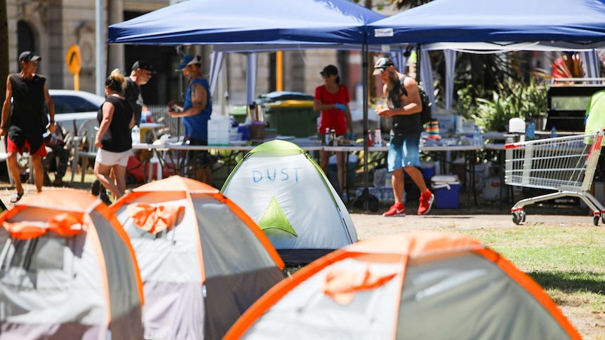 A series of one-man tents are pitched in front of two temporary gazebos serving food.