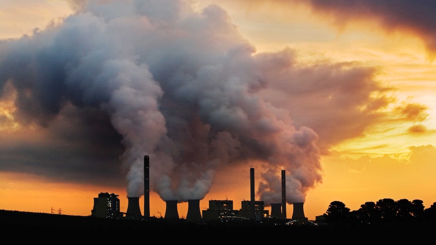 Grey smoke billowing out of power plant chimneys against orange sunset.