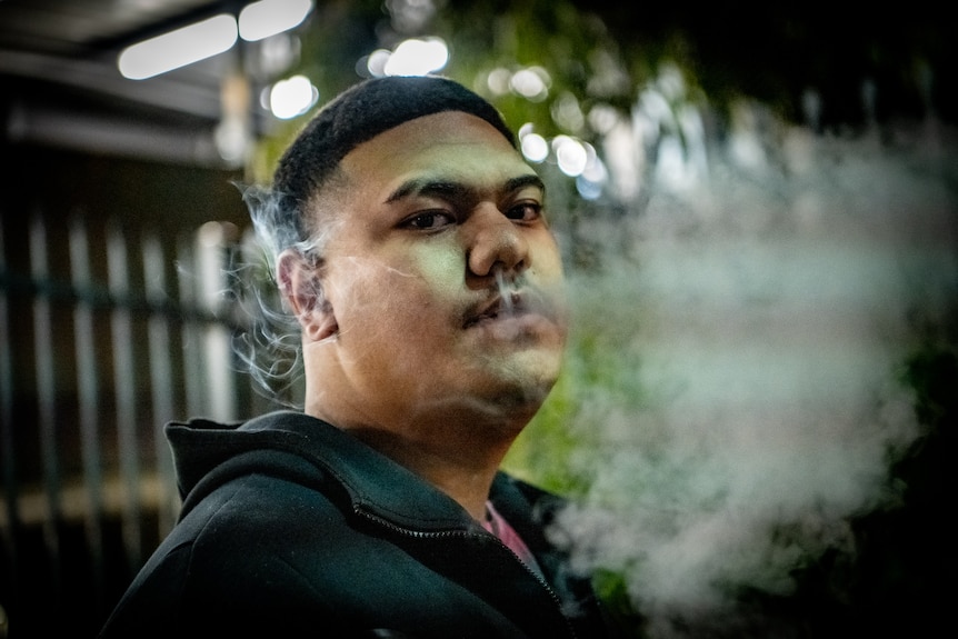 A man exhales smoke or vapour while looking at the camera.