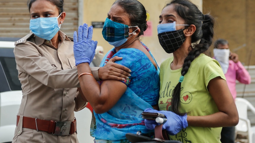 A woman in uniform holds another who is crying as she stands next to another woman watching something off camera.