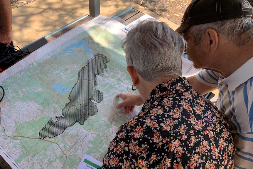 A man and a woman look at and point at a map with a big blackened area in the middle
