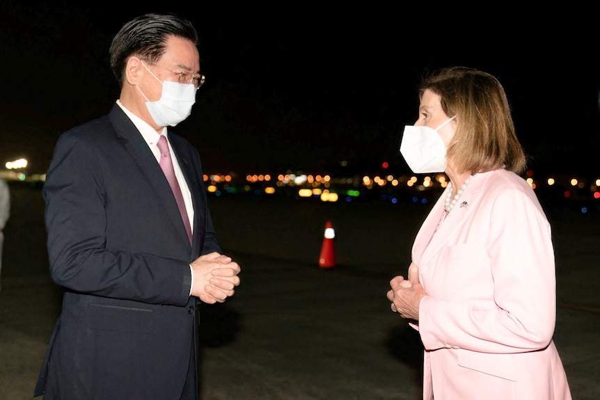 El ministro de Relaciones Exteriores de Taiwán, Joseph Wu, vestido con un traje y una máscara, recibe a Nancy Pelosi con un traje rosa y una máscara.
