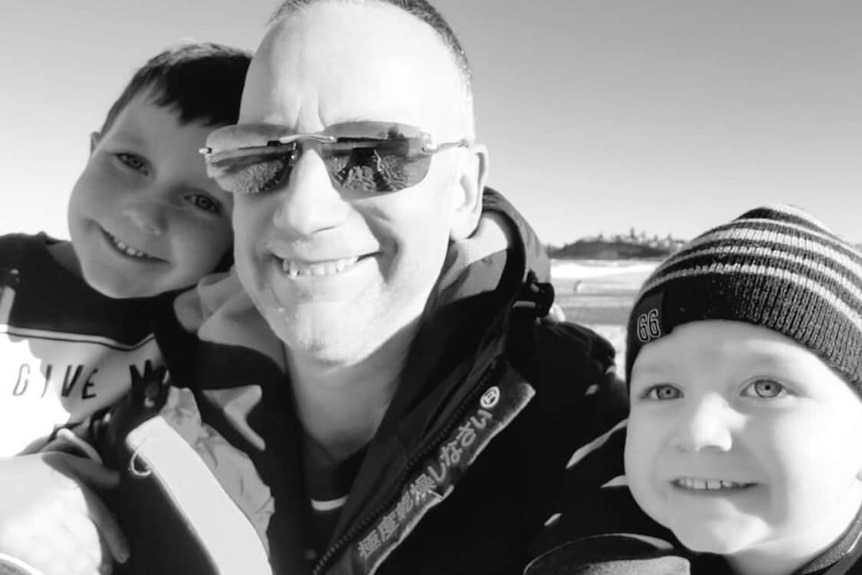 A dad in sunglasses takes a selfie with two young boys