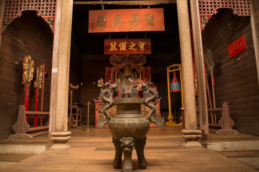 A shrine to Hou Wang sits atop an altar at the back of the temple. Wall hangings with Chinese characters adorn the wooden walls.