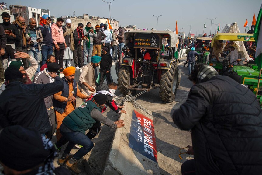 Protesting farmers remove concrete police barricades using a tractor as men push the barricades from behind.