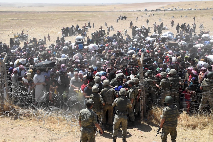 Turkish soldiers help Syrian refugees as they cross the Turkish-Syrian border