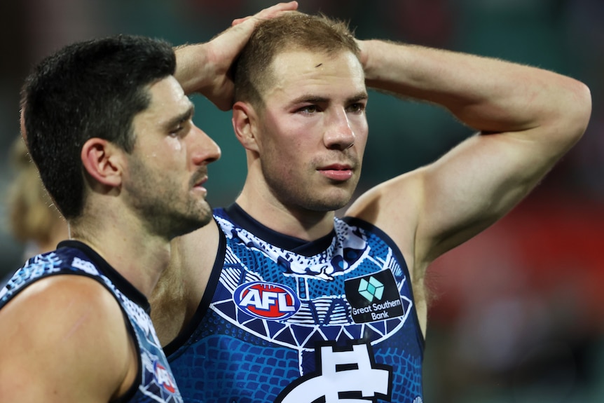 A man in a football guernsey has hands on his head and looks dejected.
