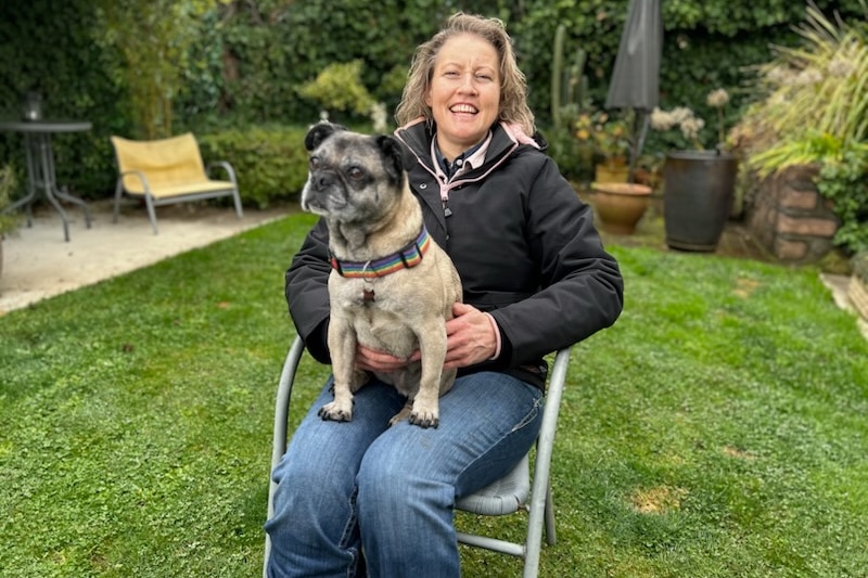 A woman sits and smiles with a dog on her lap