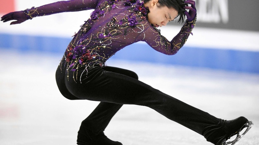 A figure skater in a purple long-sleeved shirt mid-way through a turn, with one leg pointed out.