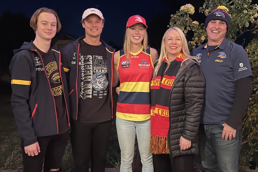 A smiling young woman stands next to her two brothers, mother and father, all of whom are wearing Adelaide Crows clothing.